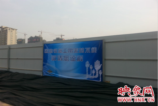 道路南側(cè)圍起了白色的圍擋，墻上標(biāo)示著“因地鐵施工帶來的不便敬請您諒解”的提示牌。