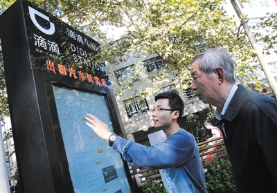 10月15日，滴滴工作人員（左）指導(dǎo)乘客使用“滴滴車站”的電子屏預(yù)約出租車。